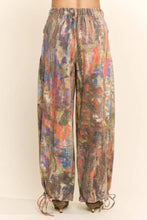 Load image into Gallery viewer, Model wearing abstract print wide leg cargo pants featuring earthy multicolor tones, oversized flap pockets, adjustable tie hems, and a relaxed fit.