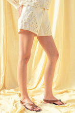 Load image into Gallery viewer, Model wearing écru tailored shorts with oversized floral appliqué embroidery paired with coordinating top in a soft neutral ivory/yellow tone.