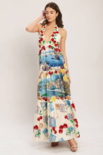 Load image into Gallery viewer, Model wearing a cream halter maxi dress featuring colorful Mediterranean coastal scenes, cherries, lemons, and postcard-inspired prints with a flowing tiered silhouette.