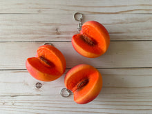 Load image into Gallery viewer, Realistic peach-shaped coin purse with zipper, keychain ring, and bag charm attachment displayed on a wood background.