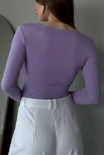 Load image into Gallery viewer, Model wearing a lavender long sleeve twist-front top with elegant draped detailing at the bust, paired with high-waisted white trousers.