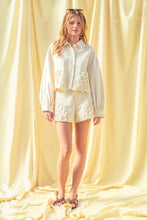 Load image into Gallery viewer, Model wearing écru tailored shorts with oversized floral appliqué embroidery paired with coordinating top in a soft neutral ivory/yellow tone.