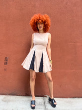Load image into Gallery viewer, A sleeveless beige mini dress featuring a boat neckline and contrast black accents peeking through the pleats, creating a chic and versatile look suitable for any occasion.