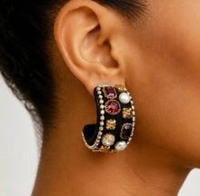 Load image into Gallery viewer, A close-up of a model's ear wearing a large, ornate gold hoop earring embellished with black velvet, faux pearls, and red gemstones.