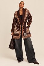 Load image into Gallery viewer, Model wearing a chocolate brown tapestry fringe cardigan with a self-tie waist belt and cream trousers.