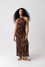Load image into Gallery viewer, Model wearing a brown floral crochet halter maxi dress with open back and semi-sheer cotton fabric, styled for summer vacation, beach getaway, or resort wear look.