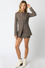 Load image into Gallery viewer, Woman wearing a plaid blazer and skirt set with white boots on a white background