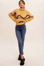 Load image into Gallery viewer, Woman wearing a mustard yellow sweater with black abstract patterns and blue jeans on a white background