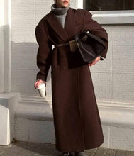 Load image into Gallery viewer, Person wearing a long brown coat with a belt, standing against a light gray wall.