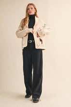 Load image into Gallery viewer, Woman wearing a beige embroidered jacket and black pants on a beige background