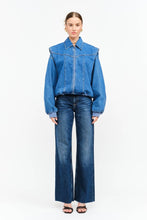 Load image into Gallery viewer, Model wearing an indigo denim bomber jacket with structured shoulders, zip-front closure, elastic hem, and gathered cuffs against a white background.