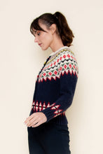 Load image into Gallery viewer, A woman wearing a navy blue Fair Isle cardigan sweater with red, green, yellow, and white patterned detailing across the chest, sleeves, and hem, styled against a neutral background.