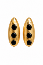 Load image into Gallery viewer, Gold-tone sculptural statement earrings with three glossy black circular accents displayed on a jewelry stand.