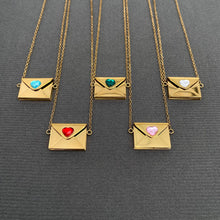 Load image into Gallery viewer, Five gold chain necklaces with envelope-shaped pendants are arranged on a dark gray textured background. Each pendant has a small heart-shaped inlay in a different color: light blue, green, white, red, and pink.