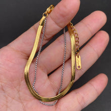 Load image into Gallery viewer, Two-tone layered bracelet featuring a flat 18K gold-plated herringbone chain alongside a delicate silver-tone link chain, with lobster clasp and adjustable extender, displayed on gray fabric.