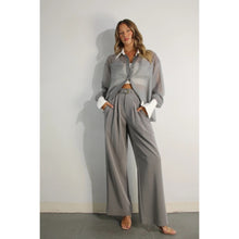 Load image into Gallery viewer, A model showcases a pair of high-waisted, grey pleated trousers, complete with a matching belt, exuding a timeless and sophisticated aesthetic. The trousers feature a tailored fit with front pleats and a straight-leg silhouette, offering both comfort and elegance. Paired with a sheer organza blouse, the ensemble presents a harmonious blend of textures and styles, perfect for both professional and formal occasions.
