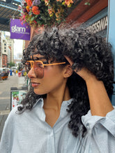 Load image into Gallery viewer, Model wearing oversized rose gold aviator sunglasses with peach-toned frames and tinted lenses, standing outside Glam Expressway boutique in DUMBO, Brooklyn, surrounded by vibrant storefront signage and flowers.