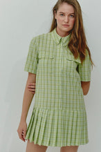 Load image into Gallery viewer, A model showcases a green checkered pleated mini dress with a box pleat design, exuding a blend of classic charm and contemporary style. The vibrant green check pattern adds a fresh pop of color, making it an ideal choice for spring and summer outings. The mini length and tailored fit highlight a playful yet sophisticated silhouette, perfect for casual gatherings, picnics, or brunches.