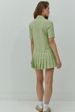 Load image into Gallery viewer, A model showcases a green checkered pleated mini dress with a box pleat design, exuding a blend of classic charm and contemporary style. The vibrant green check pattern adds a fresh pop of color, making it an ideal choice for spring and summer outings. The mini length and tailored fit highlight a playful yet sophisticated silhouette, perfect for casual gatherings, picnics, or brunches.