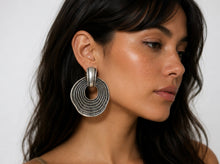 Load image into Gallery viewer, Oversized silver statement earrings featuring layered circular ring detailing and an oxidized textured finish displayed on a model.