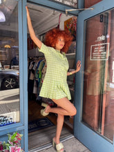 Load image into Gallery viewer, A model showcases a green checkered pleated mini dress with a box pleat design, exuding a blend of classic charm and contemporary style. The vibrant green check pattern adds a fresh pop of color, making it an ideal choice for spring and summer outings. The mini length and tailored fit highlight a playful yet sophisticated silhouette, perfect for casual gatherings, picnics, or brunches.