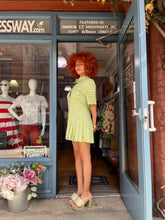Load image into Gallery viewer, A model showcases a green checkered pleated mini dress with a box pleat design, exuding a blend of classic charm and contemporary style. The vibrant green check pattern adds a fresh pop of color, making it an ideal choice for spring and summer outings. The mini length and tailored fit highlight a playful yet sophisticated silhouette, perfect for casual gatherings, picnics, or brunches.