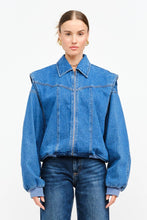 Load image into Gallery viewer, Model wearing an indigo denim bomber jacket with structured shoulders, zip-front closure, elastic hem, and gathered cuffs against a white background.