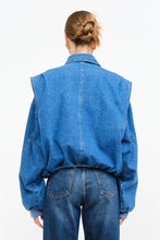 Load image into Gallery viewer, Model wearing an indigo denim bomber jacket with structured shoulders, zip-front closure, elastic hem, and gathered cuffs against a white background.