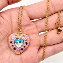 Load image into Gallery viewer, Heart-shaped pendant with colorful stones on a gold chain held in a hand.