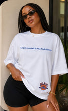 Load image into Gallery viewer, Model wearing an oversized white premium graphic T-shirt featuring the phrase "Largest Comeback in Finals History" with a small Glam Expressway logo detail, styled with black biker shorts and sunglasses.
