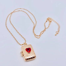 Load image into Gallery viewer, 14K gold-plated rectangular locket necklace with a red heart-shaped stone and radiating etched design on a delicate gold chain.