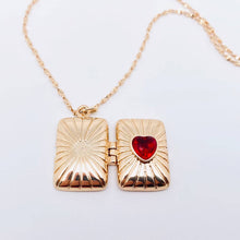 Load image into Gallery viewer, 14K gold-plated rectangular locket necklace with a red heart-shaped stone and radiating etched design on a delicate gold chain.