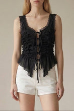 Load image into Gallery viewer, Model wearing a black sleeveless ruched lace tie top with intricate front ruching, lace trim and adjustable tie front paired with white shorts.