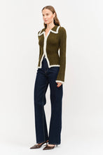 Load image into Gallery viewer, Model wearing olive green fitted double-zip knit top with ivory fuzzy trim, long sleeves, and pointed collar, styled with dark-wash wide-leg jeans.”