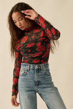 Load image into Gallery viewer, Person wearing Glam Expressway's red and black floral long-sleeve bodysuit top with blue jeans on a beige background