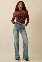 Load image into Gallery viewer, Woman wearing Glam Expressway's red and black floral top with blue jeans on a beige background