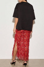 Load image into Gallery viewer, Model wearing a vibrant red sequin fringe midi skirt featuring intricate embellishments and textured tassel detailing paired with an oversized black t-shirt.