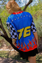 Load image into Gallery viewer, Woman wearing the All American Racing Team oversized mesh jersey featuring blue racing graphics, checkered sleeves, flame details, varsity lettering, and a large number 76 on the back.