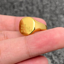 Load image into Gallery viewer, Gold ring with 'The World is Yours' engraving on a finger against a blurred background