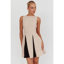 Load image into Gallery viewer, A sleeveless beige mini dress featuring a boat neckline and contrast black accents peeking through the pleats, creating a chic and versatile look suitable for any occasion.