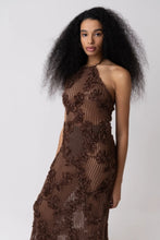 Load image into Gallery viewer, Model wearing a brown floral crochet halter maxi dress with open back and semi-sheer cotton fabric, styled for summer vacation, beach getaway, or resort wear look.