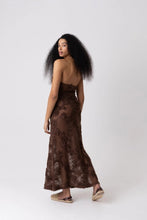 Load image into Gallery viewer, Model wearing a brown floral crochet halter maxi dress with open back and semi-sheer cotton fabric, styled for summer vacation, beach getaway, or resort wear look.