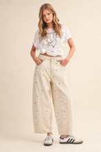 Load image into Gallery viewer, Model wearing cream barrel-leg jeans embellished with silver stud details throughout, featuring a high-rise waist and relaxed statement silhouette.