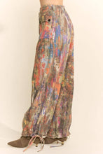 Load image into Gallery viewer, Model wearing abstract print wide leg cargo pants featuring earthy multicolor tones, oversized flap pockets, adjustable tie hems, and a relaxed fit.