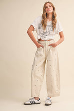 Load image into Gallery viewer, Model wearing cream barrel-leg jeans embellished with silver stud details throughout, featuring a high-rise waist and relaxed statement silhouette.