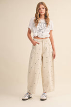 Load image into Gallery viewer, Model wearing cream barrel-leg jeans embellished with silver stud details throughout, featuring a high-rise waist and relaxed statement silhouette.