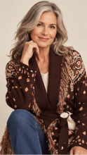 Load image into Gallery viewer, Model wearing a chocolate brown tapestry fringe cardigan with a self-tie waist belt and cream trousers.