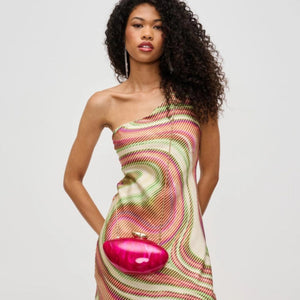 Woman wearing a colorful one-shoulder dress holding a pink clutch against a white background