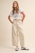 Load image into Gallery viewer, Model wearing cream barrel-leg jeans embellished with silver stud details throughout, featuring a high-rise waist and relaxed statement silhouette.
