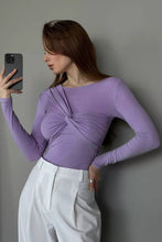 Load image into Gallery viewer, Model wearing a lavender long sleeve twist-front top with elegant draped detailing at the bust, paired with high-waisted white trousers.
